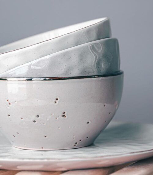 Vaisselle en porcelaine artisanale aux tons clairs, empilée sur une assiette, pour une décoration intérieure élégante et minimaliste