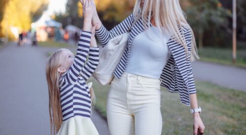 Maman quadra élégante partageant une glace avec sa fille lors d’une balade en plein air, complicité et douceur au coucher du soleil.