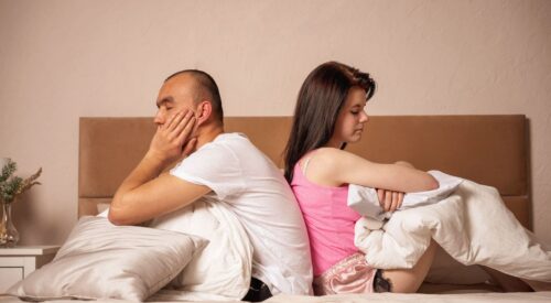 Couple dans un lit dos à dos avec des oreillers, illustrant la baisse de libido et les tensions dans le couple liées à la charge mentale et à la fatigue du quotidien.