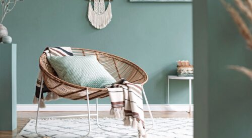 Intérieur slow maison avec fauteuil en rotin, coussins verts et décoration bohème apaisante