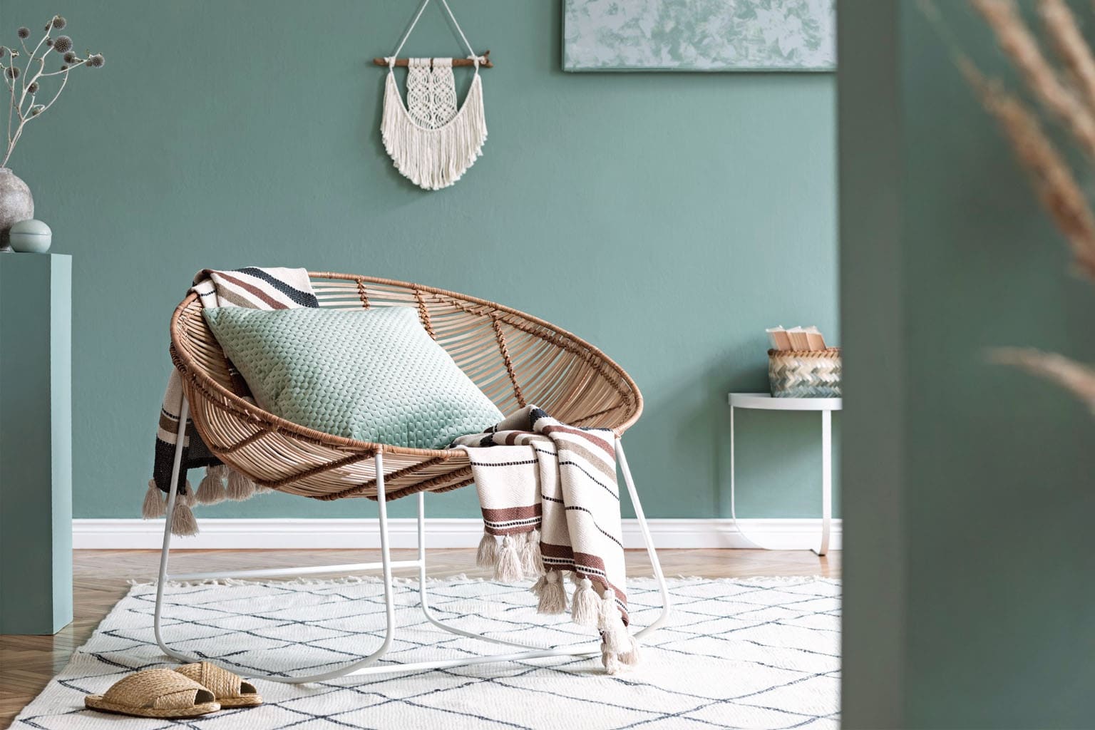 Intérieur slow maison avec fauteuil en rotin, coussins verts et décoration bohème apaisante