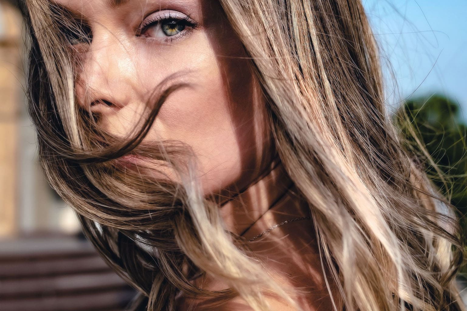 Femme aux cheveux châtains lumineux au vent, regard vert intense, beauté naturelle printemps-été 2026