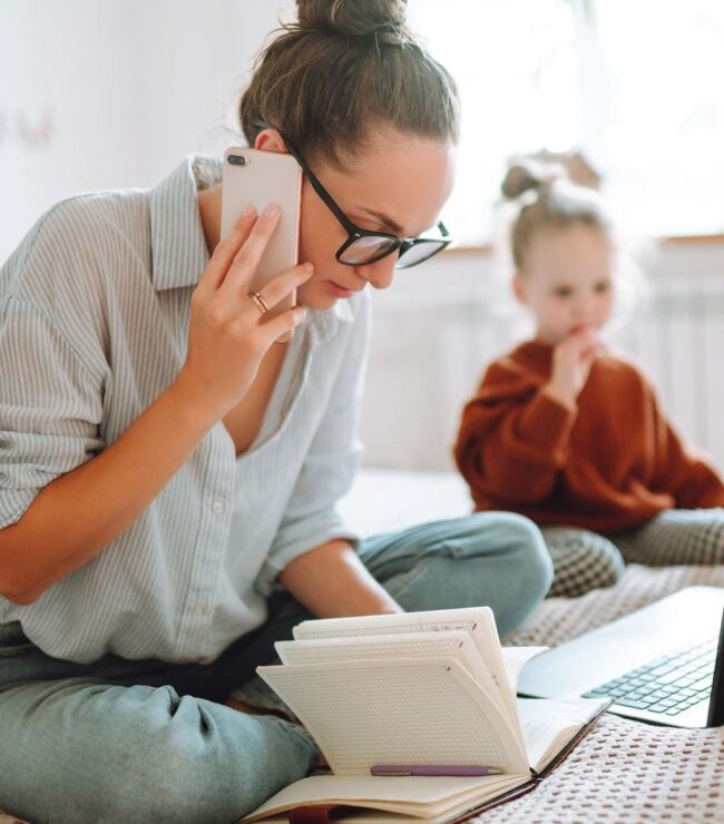 maman en télétravail avec ordinateur portable et téléphone pendant que son enfant joue à côté charge mentale working mum quotidien
