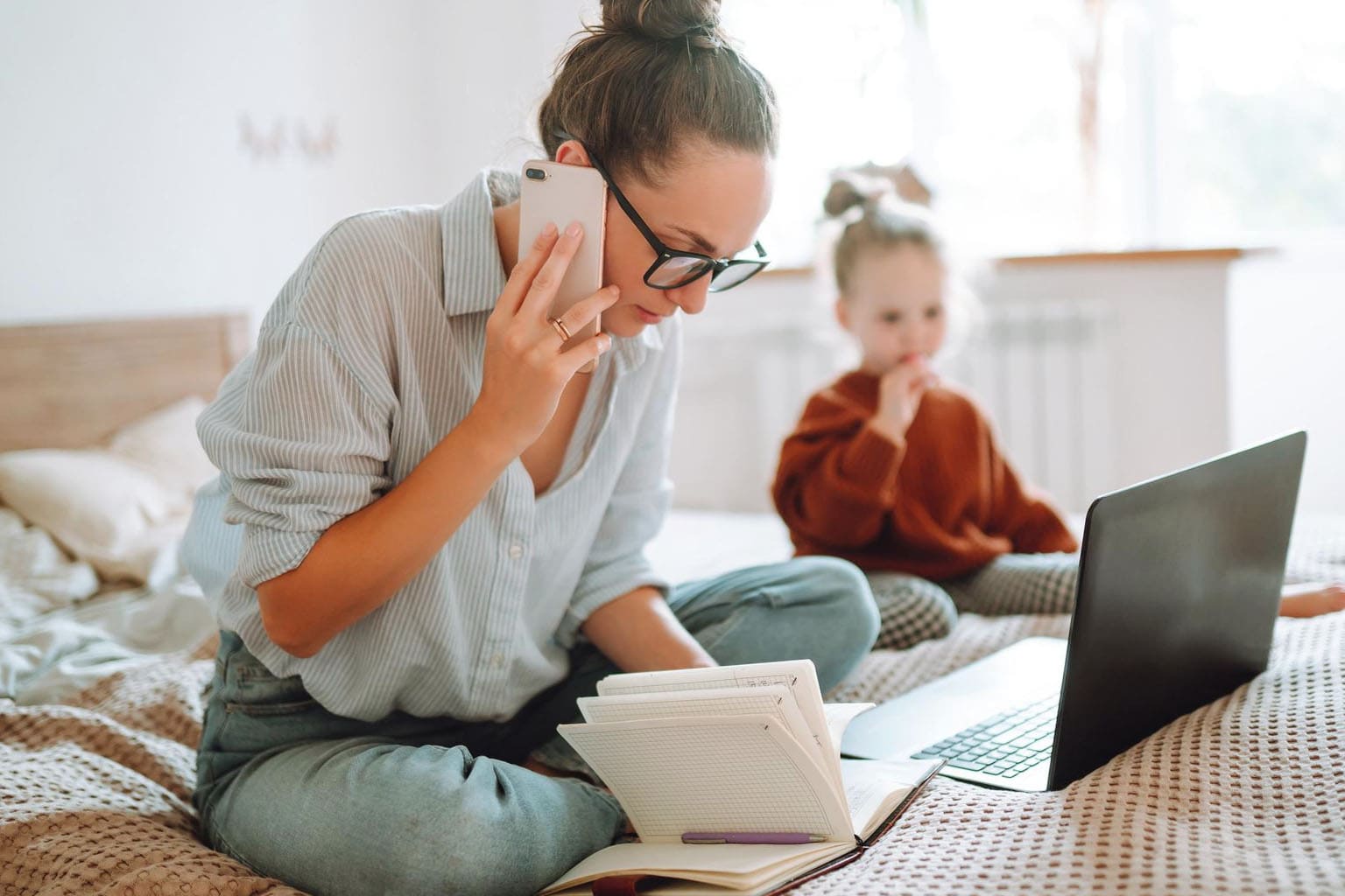 maman en télétravail avec ordinateur portable et téléphone pendant que son enfant joue à côté charge mentale working mum quotidien