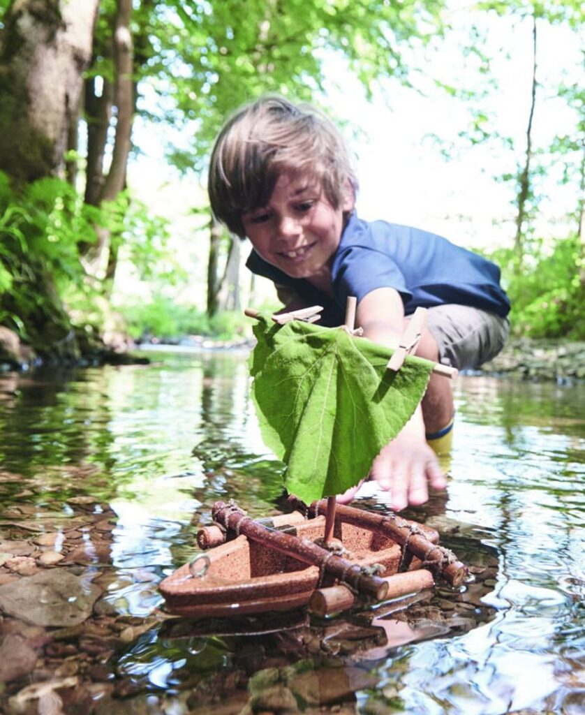 bcdjeux activite exterieur famille kit diy bateau Enfant jouant dans l’eau avec un bateau fait main en bois et feuilles, activité nature créative pour jouer dehors en famille