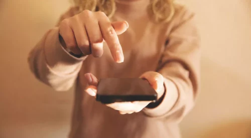 Femme aux cheveux bouclés tenant un smartphone dans ses mains, illustration de la charge mentale numérique, de l'hyperconnexion et de la quête d'un quotidien plus slow.