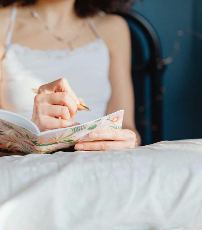 Femme écrivant dans un carnet au lit pour raconter son histoire et ses souvenirs