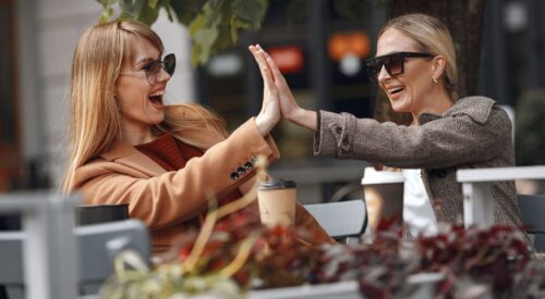 Deux femmes de 40 ans souriantes en terrasse de café partageant un moment de complicité et de liberté après la quarantaine