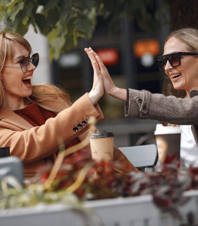 Deux femmes de 40 ans souriantes en terrasse de café partageant un moment de complicité et de liberté après la quarantaine
