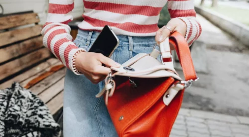 Femme cherchant un objet dans son sac, symbole du quotidien d'une maman hybride qui jongle entre ses multiples rôles de mère, salariée et femme active.