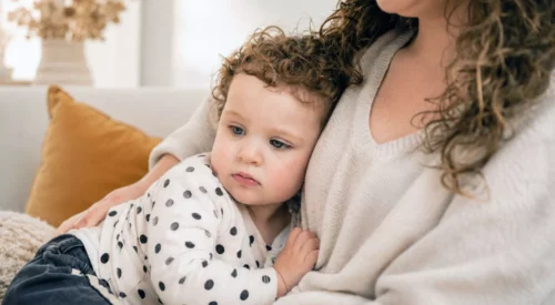 Maman tenant sa fille de 2 ans contre elle sur un canapé, illustrant la perte d'identité et le lien fusionnel après la naissance.