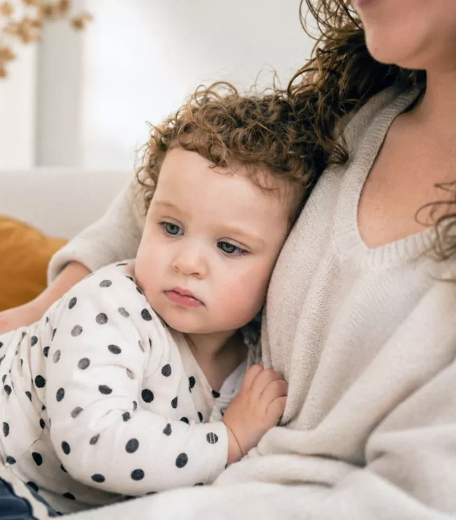 Maman tenant sa fille de 2 ans contre elle sur un canapé, illustrant la perte d'identité et le lien fusionnel après la naissance.