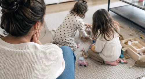 Maman regardant ses 2 petites filles jouer au sol, après plusieurs années consacrées à ses enfants avant son retour au travail.