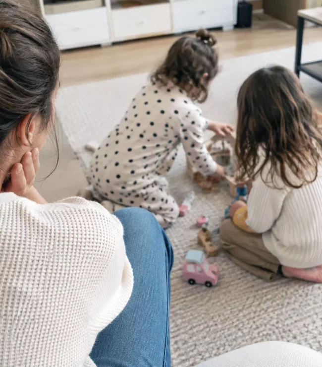 Maman regardant ses 2 petites filles jouer au sol, après plusieurs années consacrées à ses enfants avant son retour au travail.