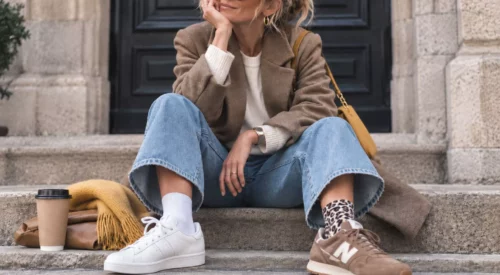 Femme assise sur des marches avec jean large, baskets dépareillées et accessoires jaunes