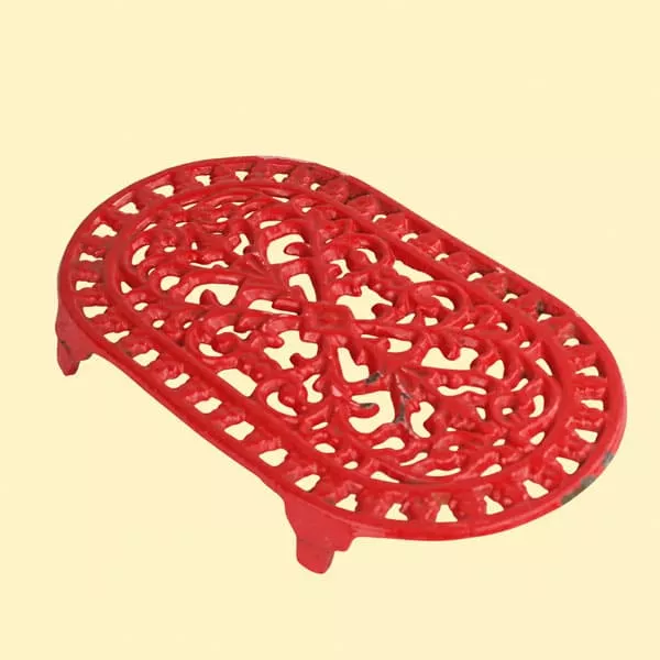 dessous de plat emmau art de la table inspiration sud france Dessous-de-plat ovale rouge en fonte émaillée à motifs ajourés sur fond jaune pâle.