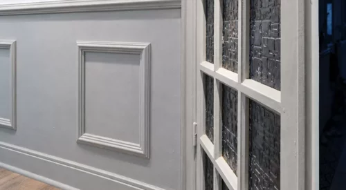 Boiseries à moulures et porte vitrée ancienne peintes en Gazelle de Dulux Valentine, avec un mur blanc au-dessus.